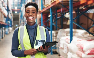 A worker in a warehouse, smiling while holding her tablet