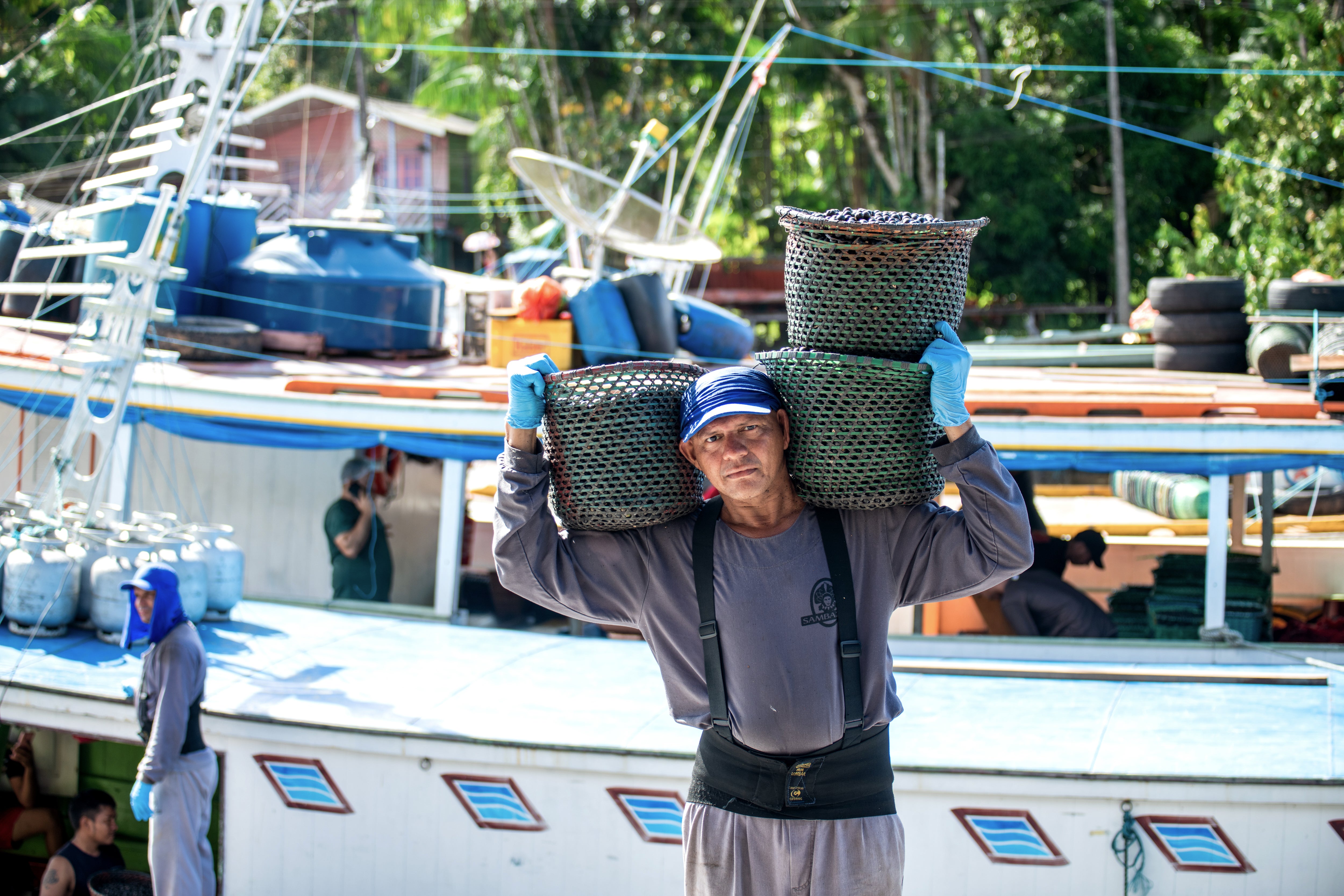 EcoEnterprises IV géré par EcoEnterprises Impact Management : Photo d’une personne tenant des paniers de produits sur chacune de ses épaules devant un bateau de travail, regardant vers la caméra.