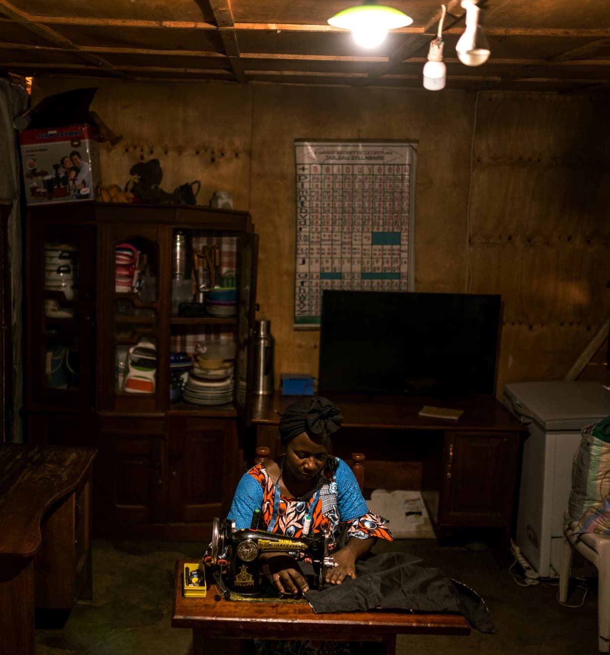 Aimé Bushinga utilise sa lanterne solaire pour coudre à la maison