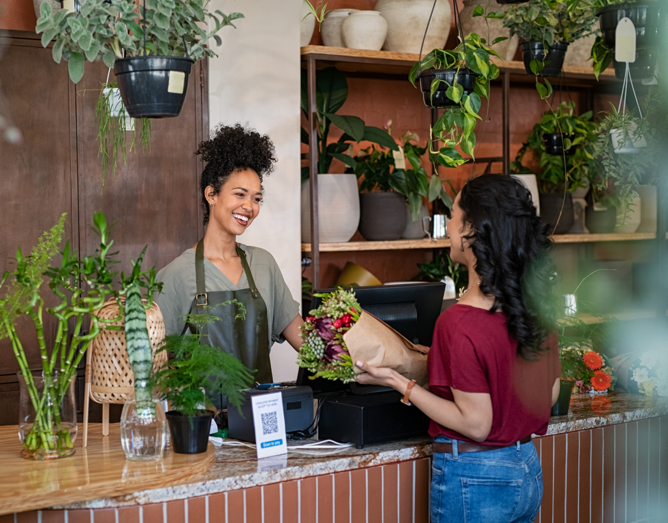 A smiling florist selling plants and flowers to a client.