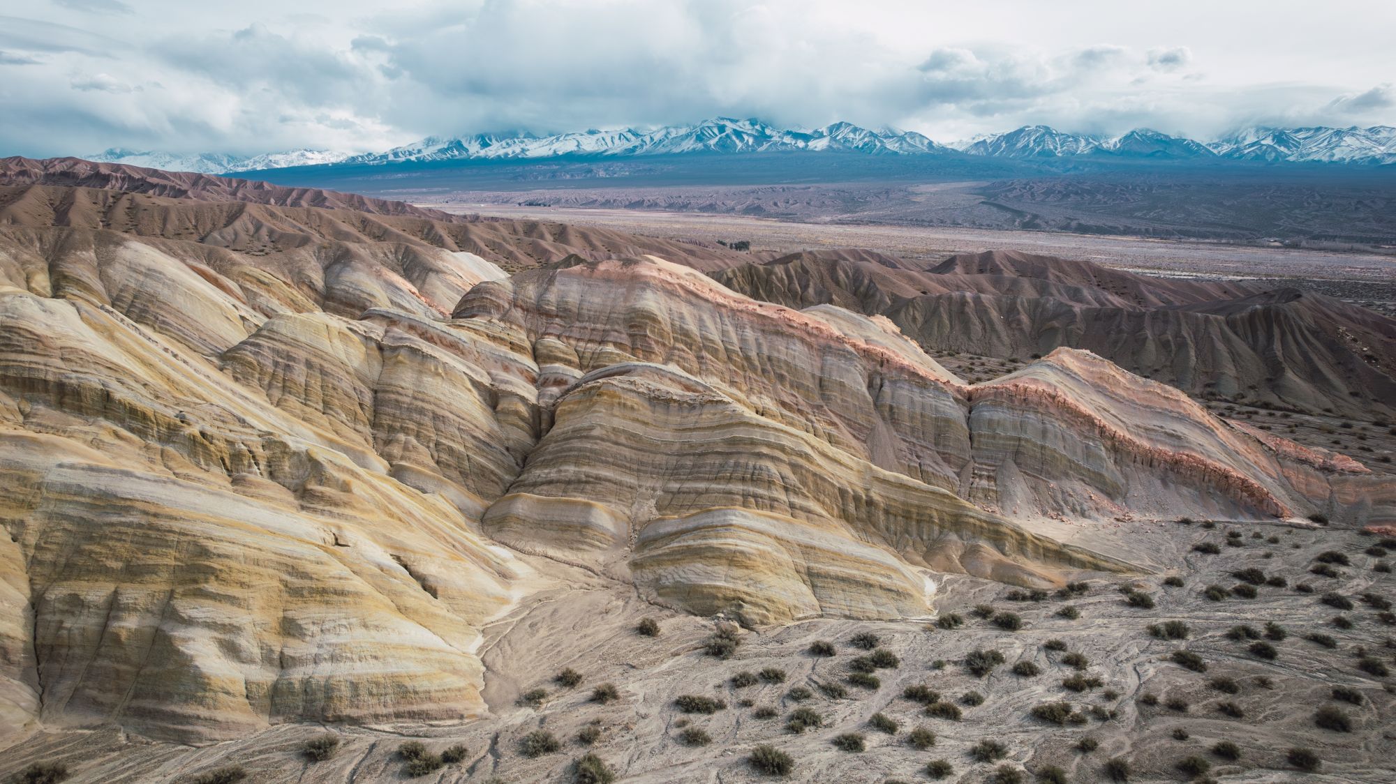 Desertic landscape with orange and ocher colored rocks, snowy mountains in the background