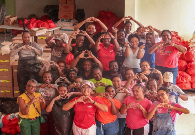 A large group of people making heart shapes with their hands, surrounded by bags and boxes of supplies.